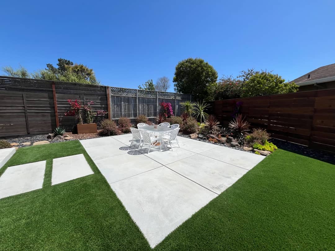 A back garden with artificial turf, poured concrete pads, planting beds, and a new fence