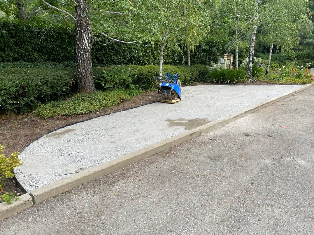 A freshly finished concrete apron curving into a driveway, with a plate compactor still on it