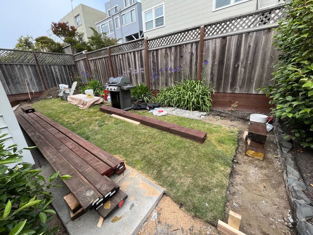 A back garden stripped out during demolition, with old deck timbers stacked across the lawn