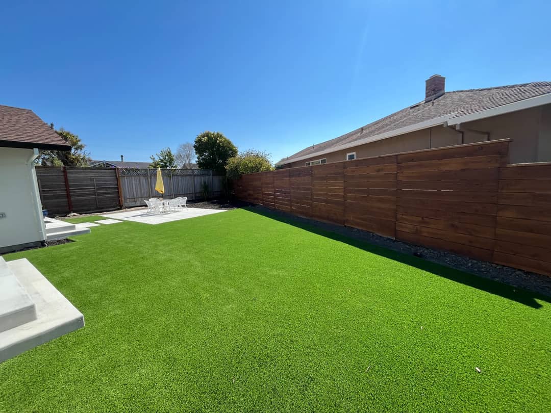 A bright artificial turf lawn in a back garden enclosed by a new horizontal redwood fence